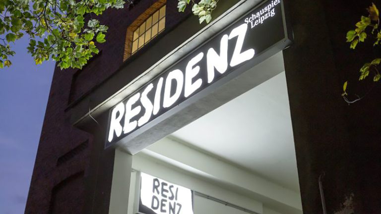Nächtliche Aufnahme des Eingang der Spielstätte mit einem leuchtenden Schild Residenz