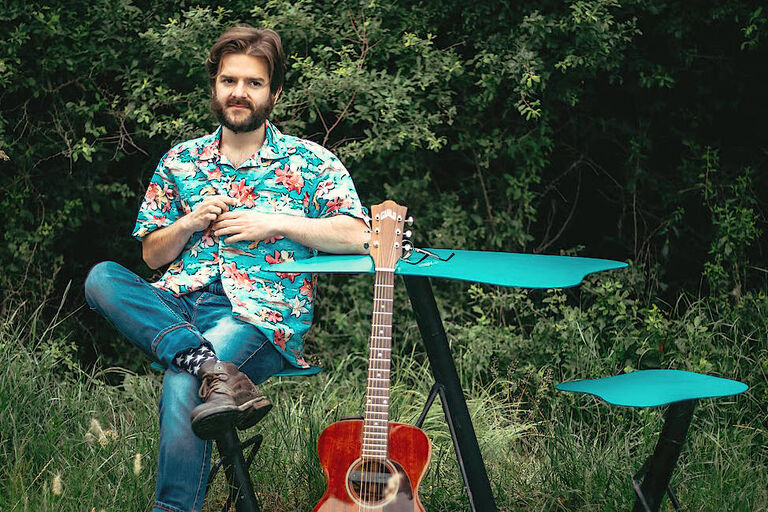 Richard Limbert sitzt auf einer grünen Wiese an einem Tich, an den seine Gitarre gelehnt ist