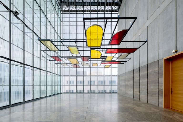 In einem hohen Lichthof des Museums hängt parallel zur Decke eine Stahlgitter mit gelben und roten Glasscheiben