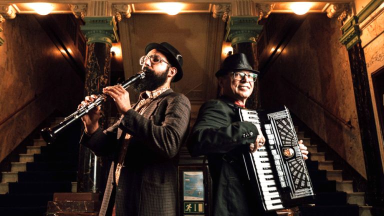Zwei Musiker mit Klarinette und Akkordeon stehen in einem historischen, herrschaftlichen Treppenhaus.