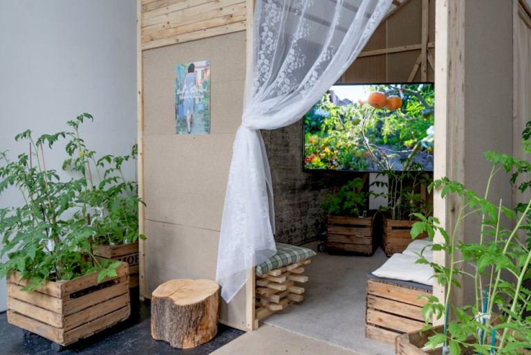 Ausstellungsansicht mit einer Holzhütte, in der auf einem Farbbildschirm Orangen zu sehen sind