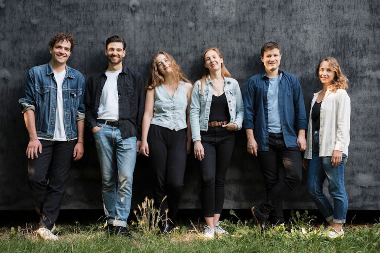 Gruppenfoto der freundlich lächelnden Sängerinnen und Sänger auf einer Wiese vor einer roh verputzten Wand