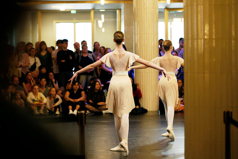 Zwei Balletttänzerinnen treten im Foyer der Oper vor zahlreichem Publikum auf.