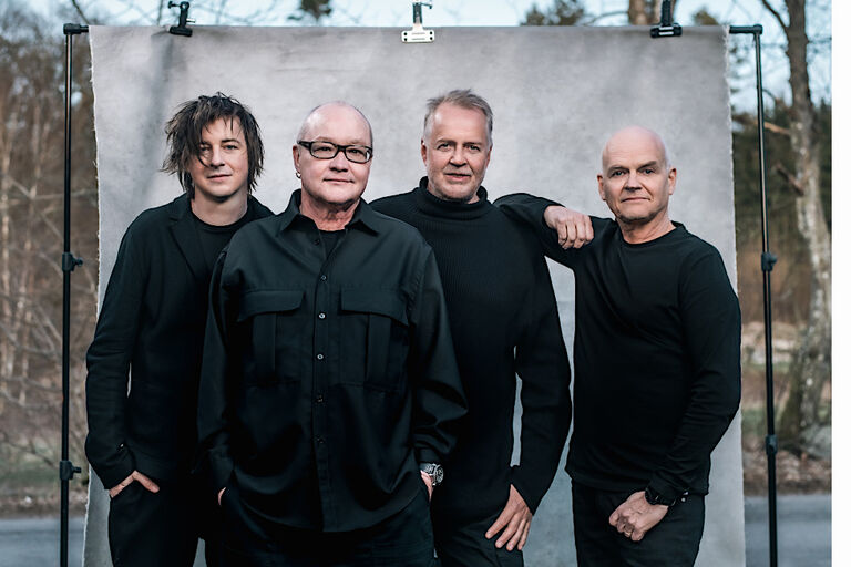Die vier Musiker auf einem Gruppenfoto vor einer Leinwand im Freien