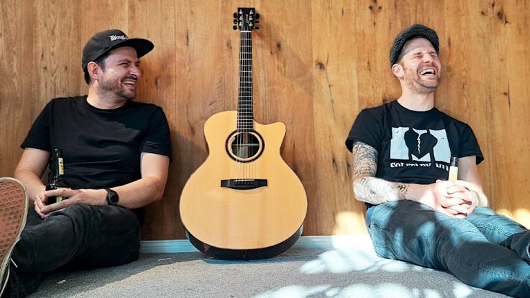 Die beiden Musiker sitzen lachend auf dem Boden mit einer Gitarre zwischen sich
