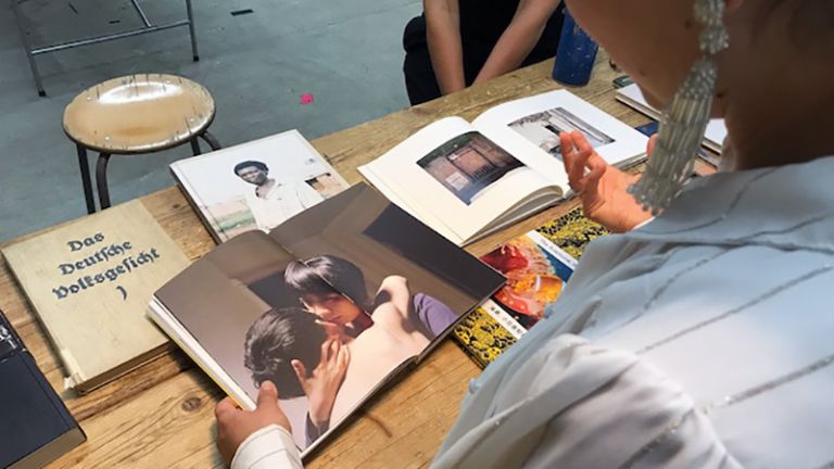 Eine Frau blättert in einem von mehreren Fotobüchern, die vor ihr auf dem Tisch liegen.
