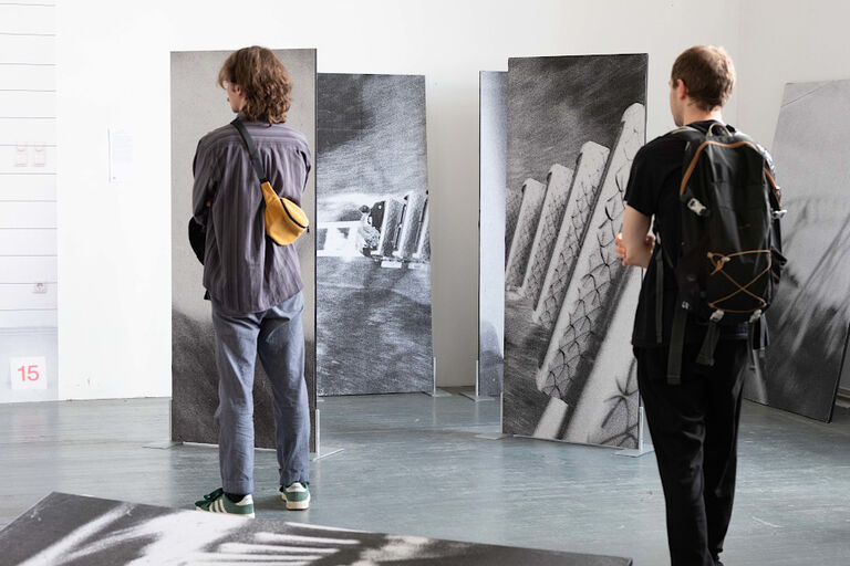 Zwei Besucher schauen in sich in einem Ausstellungsraum große Schwarz-Weiß-Fotos an.