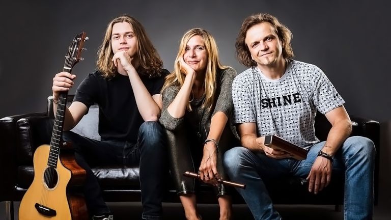 Gruppenfoto des Trios mit seinen Instrumenten auf einer schwarzen Ledercouch