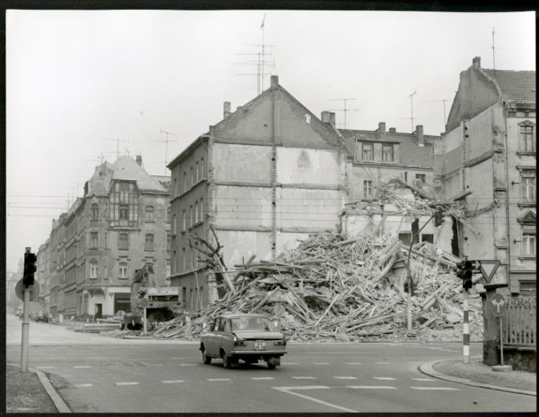 Ein Auto fährt über leere Straßen, an denen unsanierte und teilweise eingestürzte Altbauten stehen.