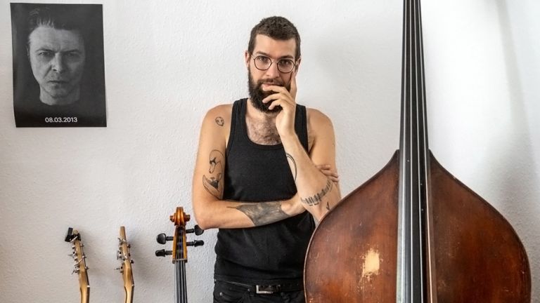Der Musiker steht in einer nachjdenklichen Haltung hinter einer Reihe von Saiteninstrumenten.