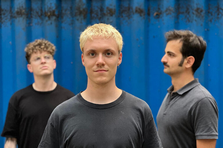 Gruppenfoto des Trios vor einem blauen Metallcontainer