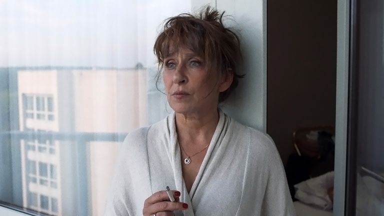 Filmszene, in der Mutter Michaela im Bademantel in ihrem Hotelzimmer steht und mit nachdenklichem Blick eine Zigarette raucht