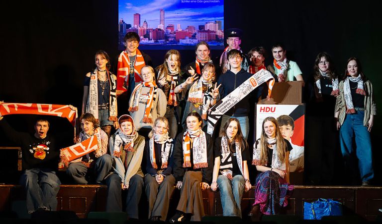 Gruppenfoto der Theatergruppe auf der Bühne in den Kostümen und der Kulisse des Stückes "Der Wohlstandskomplex"