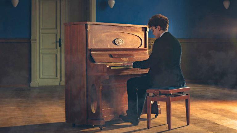 Der Musiker sitzt in einem großen, leeren Raum mit Parkettboden und spielt Klavier.