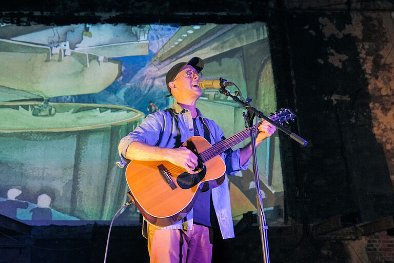 Der Sänger steht mit Gitarre bei einem Solokonzert auf der Bühne in einem alten Kino.