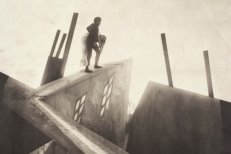 Filmszene, in der ein Mann eine leblose Frau über Dächer trägt