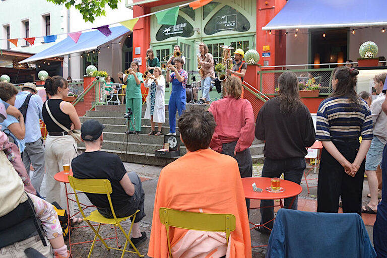 Konzert einer Band auf einer Freitreppe, das von vielen Menschen beobachtet wird