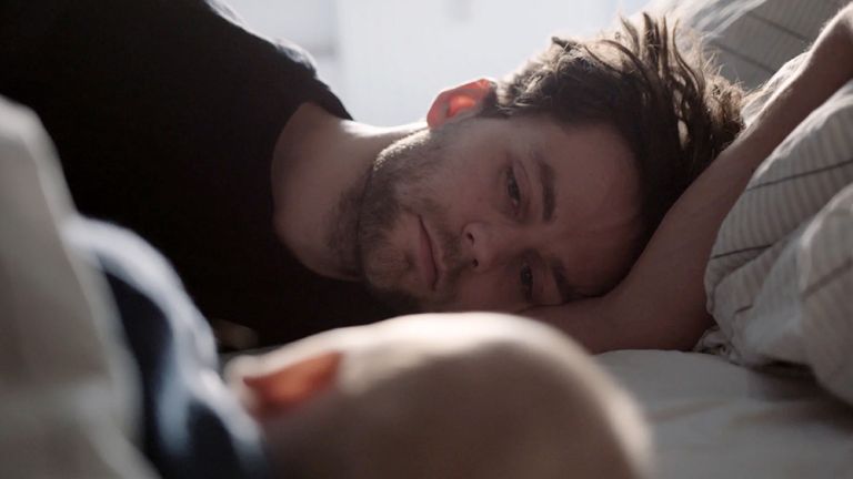 Filmszene bei der ein Vater mit seinem schlafenden Baby im Bett liegt.