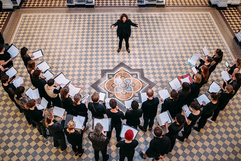 Der Chor wurde bei einem Auftritt von oben fotografiert, wie er im Halbkreis vor seinen Chorleiter steht.