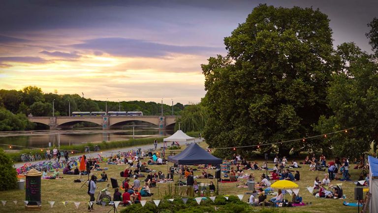 Abendliche Stimmung am Richard-Wagner-Hain und Elsterflutbecken mit vielen Menschen, Pavillions und Licherketten.
