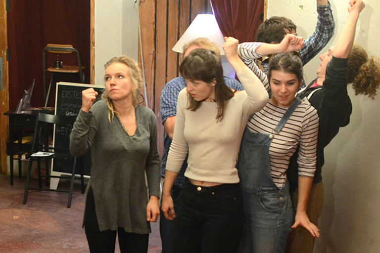 Sechs Schauspielerinnen und Schauspieler stehen in verschiedenen Posen vor einer Wand