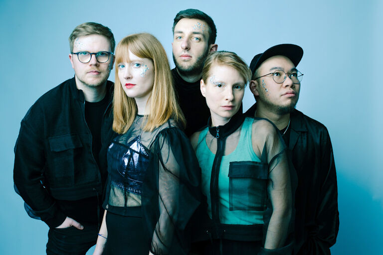 Gruppenfoto, auf dem jedes Bandmitglied Glitzer im Gesicht hat