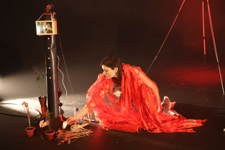 Eine Frau in rotem Umhang kniert auf der Bühne.