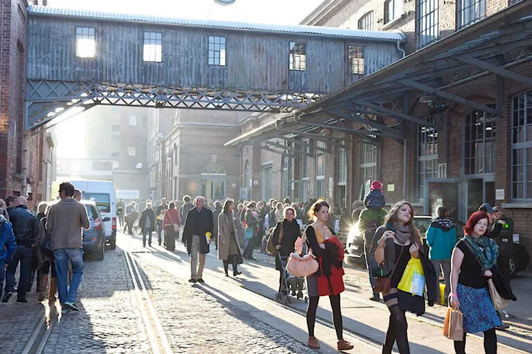 Zahlreiche Menschen sind zwischen historischen Industriegebäuden unterwegs.