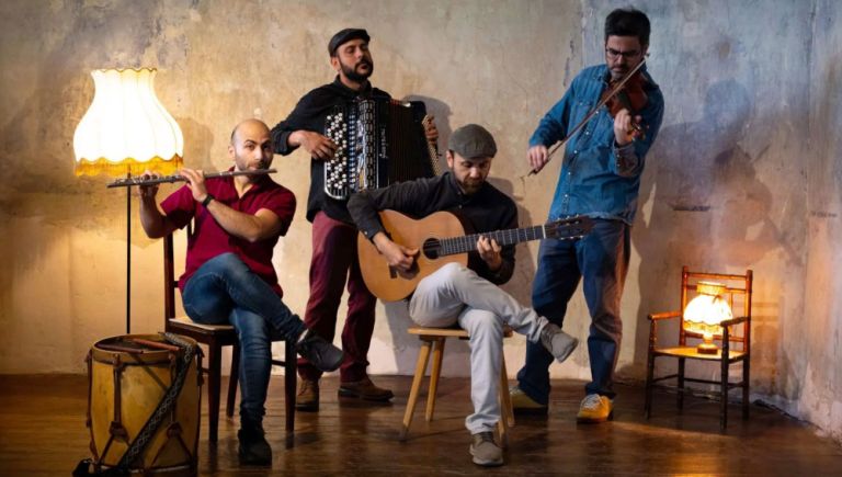 Die vier Musiker spielen in einem Zimmer, das von Stehlampen erleuchtet wird.