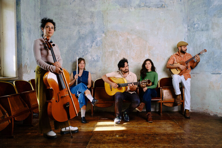 Gruppenfoto der Band in einem kahlen Raum mit hölzernen Kinossesseln an den Wänden
