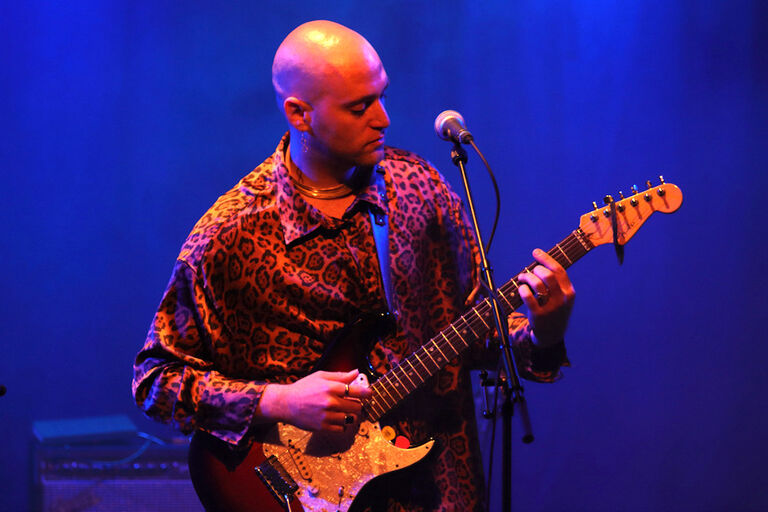 Foto des Musikers bei einem Konzert mit seiner Gitarre auf einer blau ausgeleuchteten Bühne
