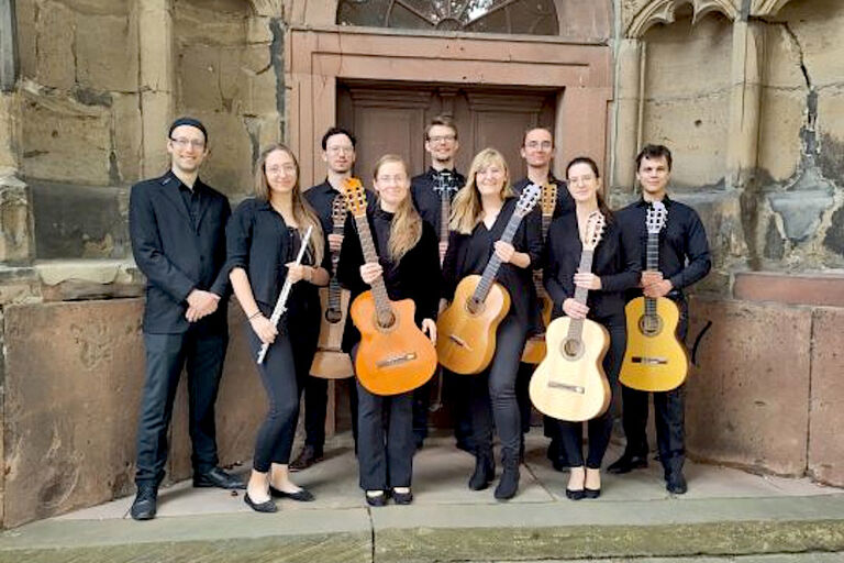 Gruppenfoto des Ensembles mit seinen Instrumenten und in schwarzer Auftrittskleidung vor einem Kirchenportal
