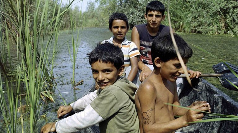 Vier Jungs fahren in einem kleinen boot durch einen naturbelassenen Flussarm.
