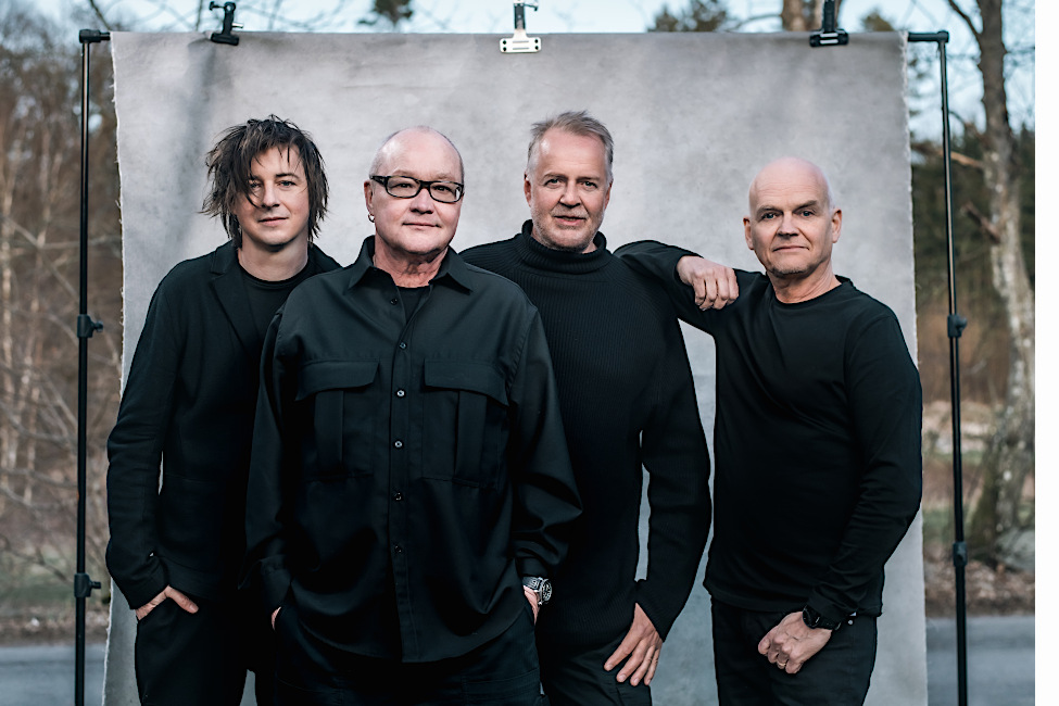 Die vier Musiker auf einem Gruppenfoto vor einer Leinwand im Freien