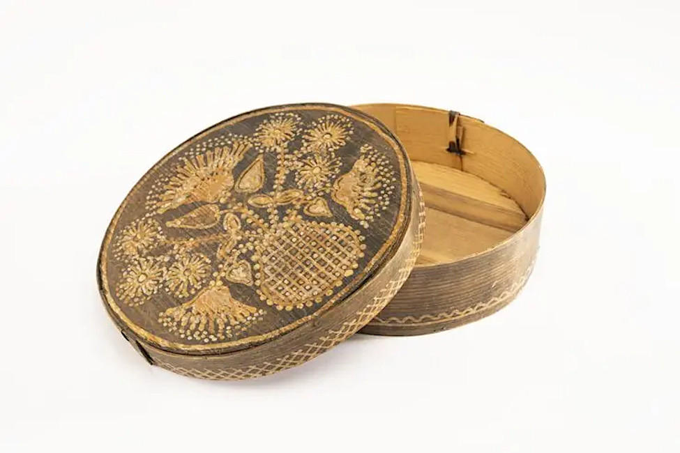 Eine runde Schachtel aus Sperrholz mit Deckel ist mit folkloristischen Motiven bemalt.