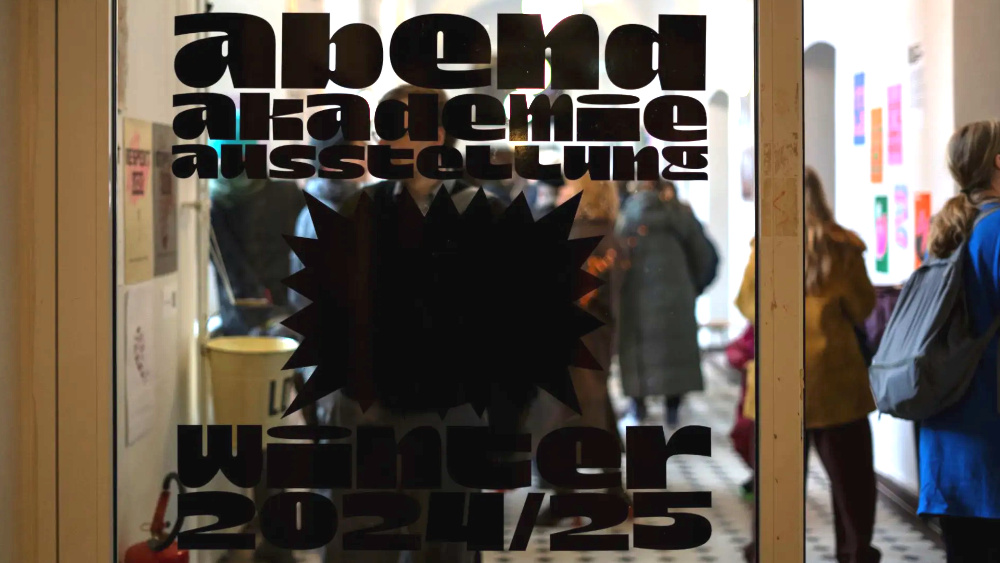Hinter einer Glastür mit der Aufschrift "abend akademie ausstellung" sind viele Menschen zu sehen, die sich Kunstwerke anschauen.