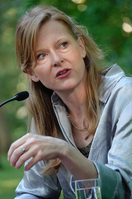 Die Autorin sitzt im Freien bei einer Lesung vor einem Mikrofon.