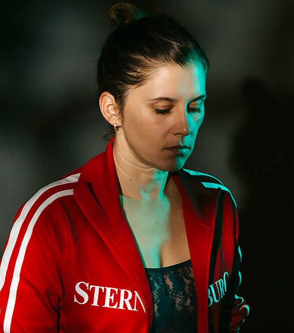 Foto der nachdenklich vor sich hin blickenden Künstlerin in roter Trainingsjacke