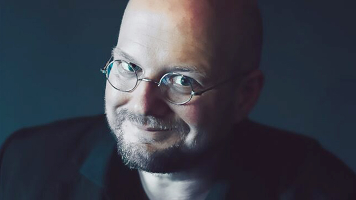 Nahaufnahme des freundlich lächelnden Autors mit Glatze und Nickelbrille