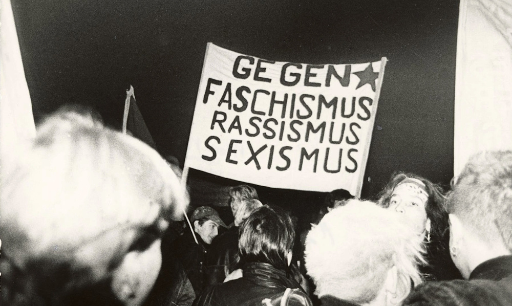 Auf einem historischen Foto tragen Jugendliche ein Transparent mit der Aufschrift: Gegen Faschismus Rassismus Sexismus.