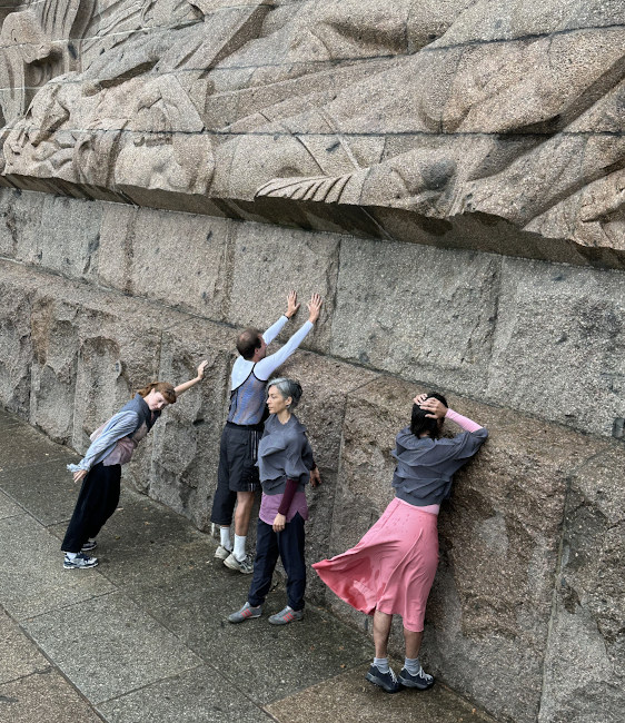 Drei Tänzerinnen und ein Tänzer stehen und lehnen in unterschiedlichen Haltungen an der Außenmauer des Völkerschlachdenkmals