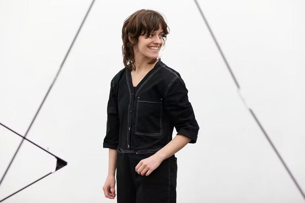 Die Choreographin steht lächelnd vor einer weißen Wanf mit großen schwarzen Dreiecken.