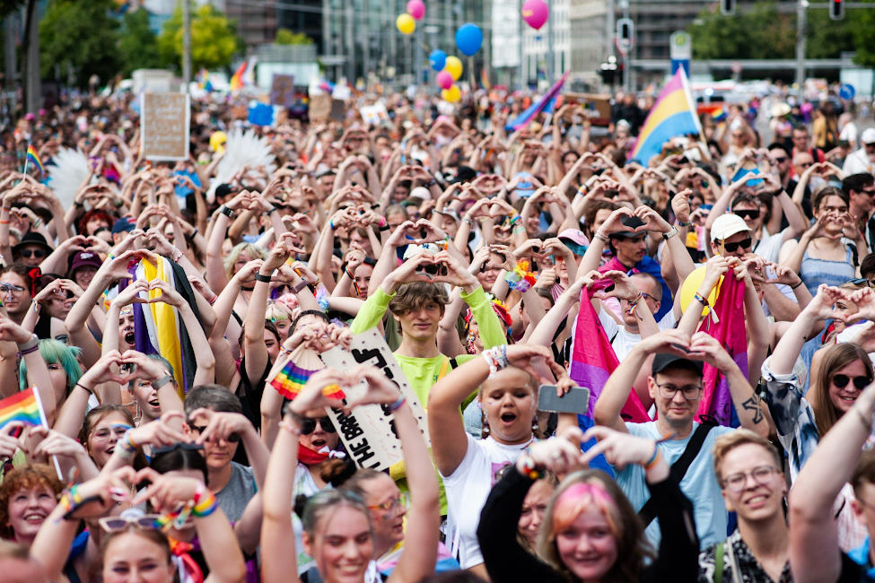 Viele fröhliche Teilnehmerinnen und Teilnehmer einer Demo formen mit ihren erhobenen Händen ein Herz.