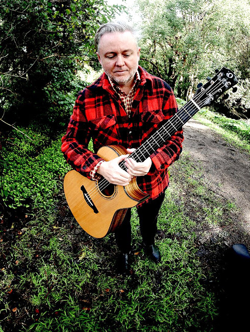 Foto des ernst vor sich hin blickenden Musikers mit seiner Gitarre im Wald