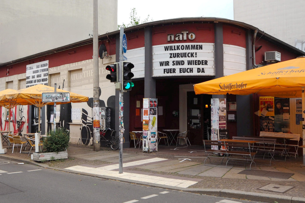 Das Gebäude der naTo mit Freisitz und Sonnenschirmen davor und mit dem Spruch "Willkommen zurück! Wir sind wieder für euch da" über dem Eingang