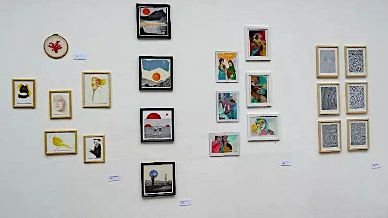 An einer weißen Wand hängen viele Bilder in kleinem Format