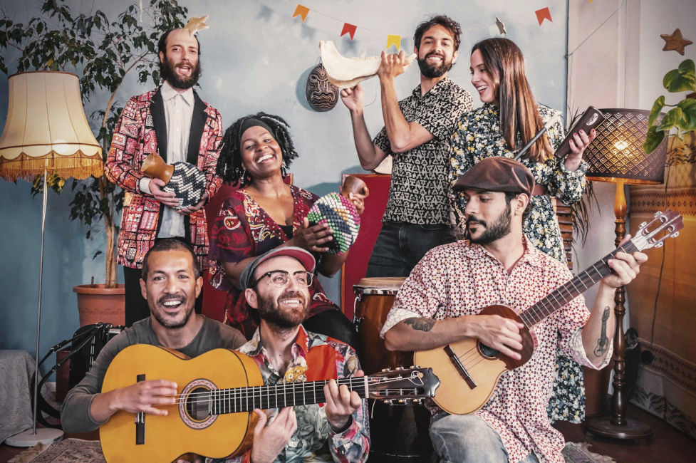 Gruppenfoto der fröhlichen Musikerinnen und Musiker mit ihren Instrumenten in einem Wohnzimmer