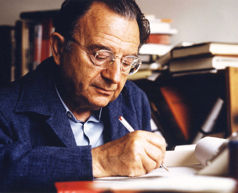 Erich Fromm sitzt mit konzentriertem Gesichtsausdruck am Schreibtich und schreibt mit einem Stift.