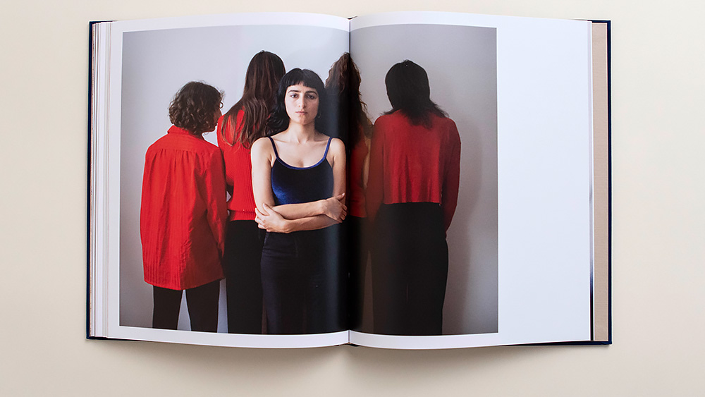 Auf der Doppelseite eines Buches ist eine Foto mit fünf Frauen zu sehen. Vier von ihnen, in roter Kleidung, stehen mit dem Rücken zum Betrachter, während eine direkt in die Kamera schaut.