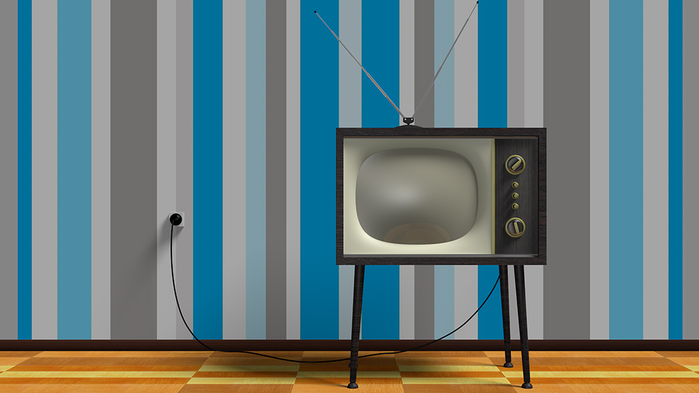 Ein historischer Röhrenfernseher steht vor einer Wand mit gestreifter Tapete.